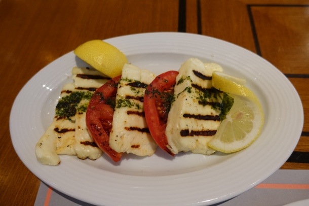 plate of grilled haloumi cheese with tomato slices and lemon wedges