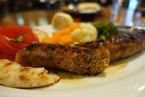 Grilled sausage cut in half and served with vegetables on a white plate